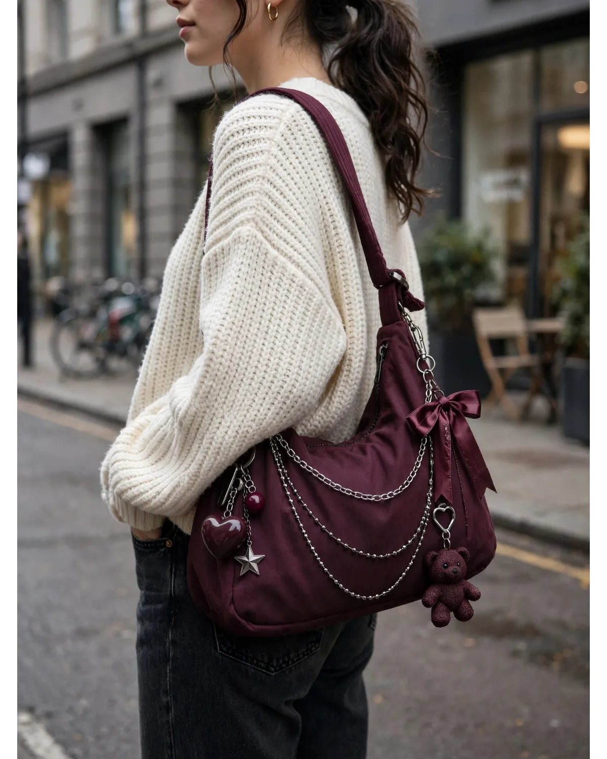 Person wearing a burgundy charm shoulder bag on a city street.
