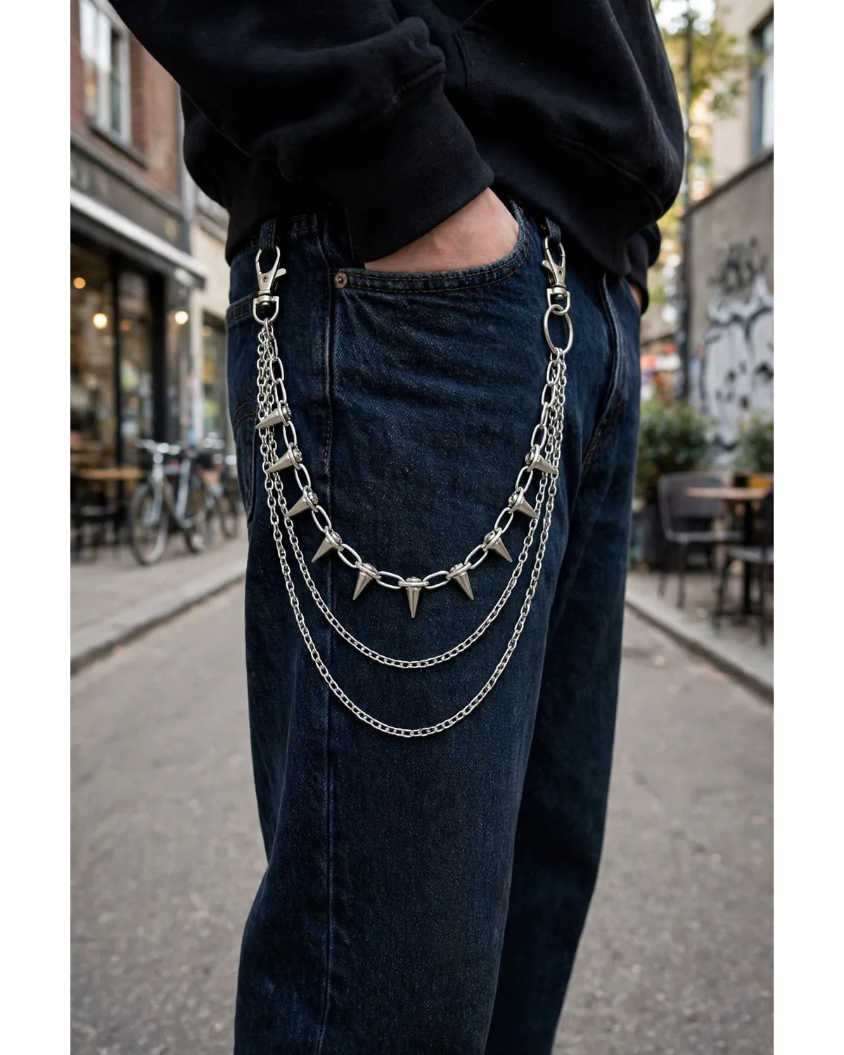 Person wearing a silver spiked triple-layer pants chain on dark jeans.