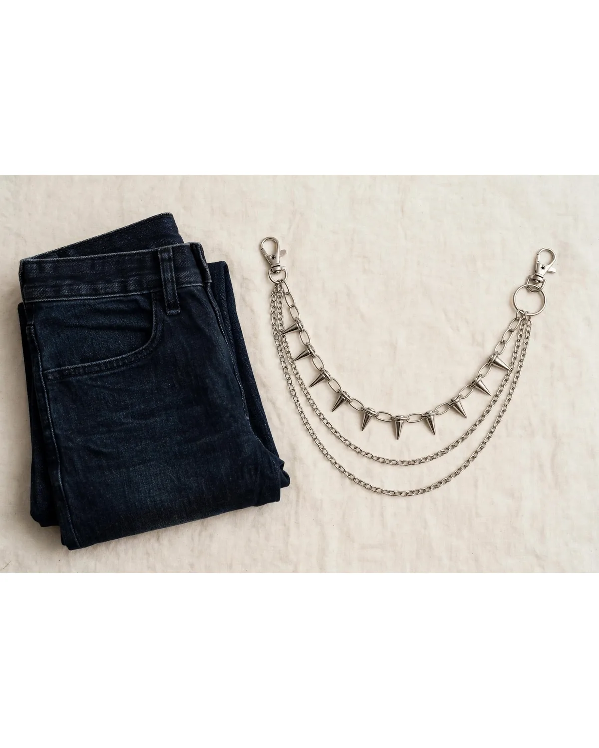 Silver spiked triple-layer pants chain laid beside folded jeans.